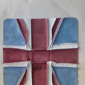 Pu&ograve; includere: Un oggetto rettangolare in pelle raffigurante la bandiera Union Jack. Il design utilizza colori blu, rosso e bianco, con una piccola etichetta al centro. L'oggetto sembra fatto a mano.