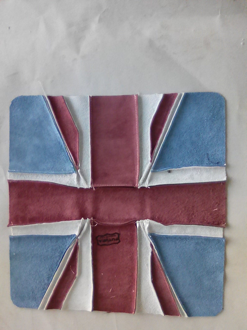 Pu&ograve; includere: Un oggetto rettangolare in pelle raffigurante la bandiera Union Jack. Il design utilizza colori blu, rosso e bianco, con una piccola etichetta al centro. L'oggetto sembra fatto a mano.