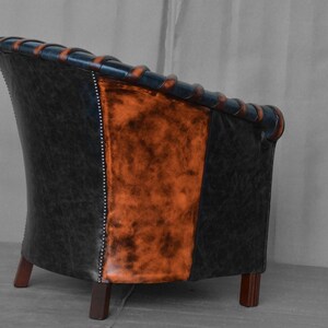 May include: A black and orange leather armchair with a tufted back and wooden legs. The chair is angled to show the side view.