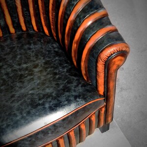 May include: A black and orange striped armchair with a tufted back and a curved, rounded seat. The chair is upholstered in a textured leather-like fabric.
