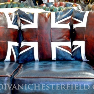 Pu&ograve; includere: Tre cuscini in pelle con il design della bandiera Union Jack, nei toni del rosso, bianco e blu, poggiano su un divano in pelle blu. I cuscini sono rettangolari e hanno una finitura invecchiata. Il divano ha un design trapuntato.