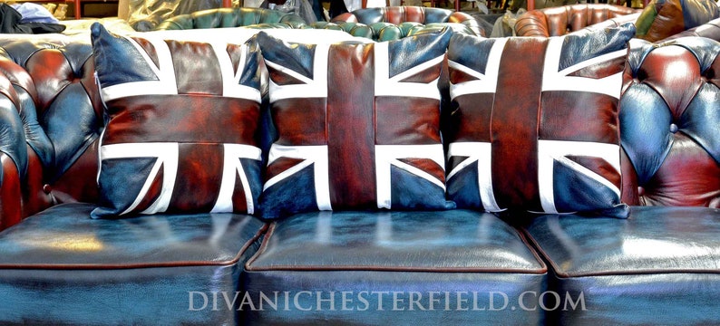 Pu&ograve; includere: Tre cuscini in pelle con il design della bandiera Union Jack, nei toni del rosso, bianco e blu, poggiano su un divano in pelle blu. I cuscini sono rettangolari e hanno una finitura invecchiata. Il divano ha un design trapuntato.