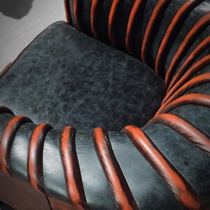 May include: A black leather armchair with orange leather piping. The chair has a unique design with the piping forming a spiral pattern.