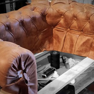 May include: Close-up of a partially constructed brown leather Chesterfield sofa. The tufted upholstery is a warm, tan color. Sewing tools and thread are visible in the foreground. The logo "HARLEQ" is in the lower left corner.