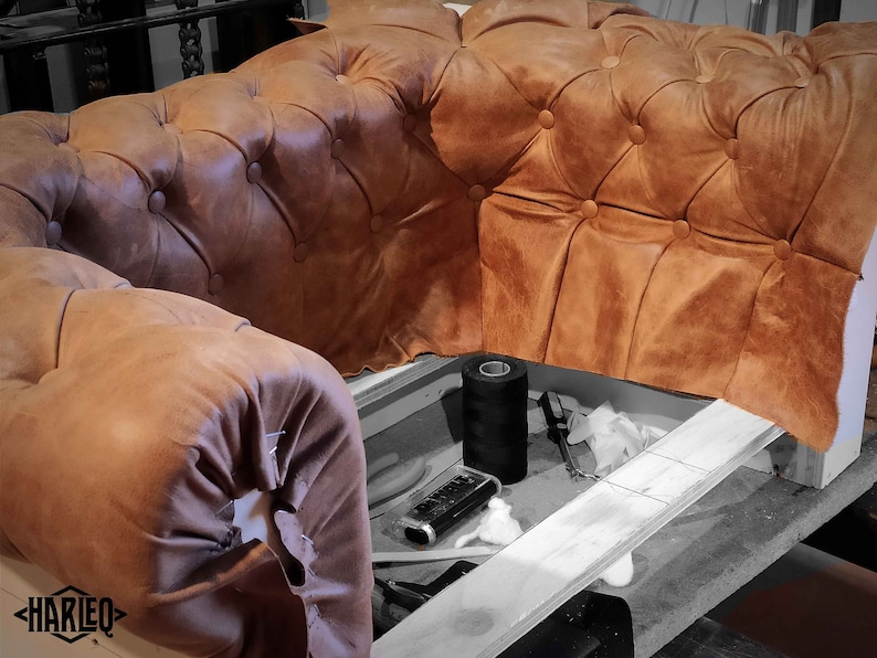 May include: Close-up of a partially constructed brown leather Chesterfield sofa. The tufted upholstery is a warm, tan color. Sewing tools and thread are visible in the foreground. The logo "HARLEQ" is in the lower left corner.