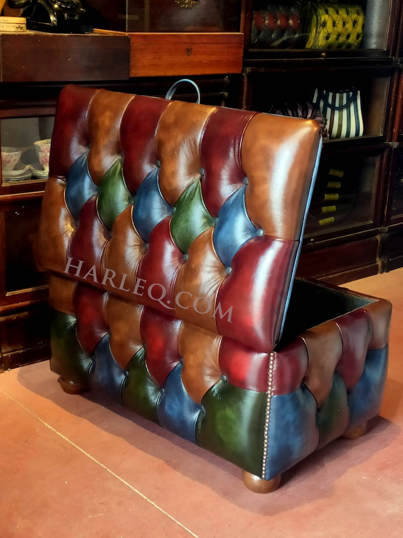 May include: A multi-colored leather storage ottoman with a tufted top and a diamond pattern. The ottoman is open and the inside is visible. The ottoman is sitting on a brown floor. HARLEQ.COM is printed on the side of the ottoman.
