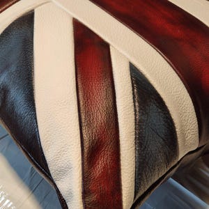 Pu&ograve; includere: Un cuscino quadrato con un design Union Jack. Il cuscino presenta strisce alternate di pelle bianca, rosso scuro, nera e bianca. La pelle ha un aspetto strutturato ed &egrave; cucita insieme.