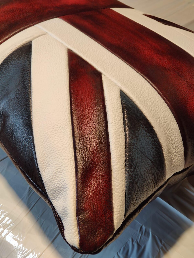 Pu&ograve; includere: Un cuscino quadrato con un design Union Jack. Il cuscino presenta strisce alternate di pelle bianca, rosso scuro, nera e bianca. La pelle ha un aspetto strutturato ed &egrave; cucita insieme.