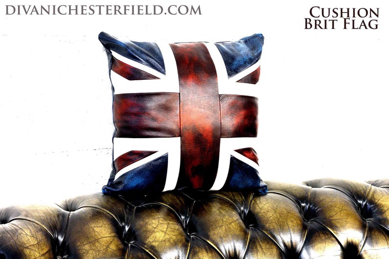 Pu&ograve; includere: Un cuscino quadrato con il design della bandiera Union Jack. Il cuscino ha un aspetto invecchiato in pelle con una combinazione di colori rosso, bianco e blu. Il testo "CUSHION BRIT FLAG" &egrave; visibile.