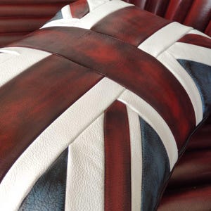 Pu&ograve; includere: Un cuscino decorativo con il design della Union Jack, nei colori bordeaux, bianco e blu navy. Il cuscino &egrave; realizzato in un materiale strutturato ed &egrave; posto su una superficie bordeaux. Il design &egrave; audace.