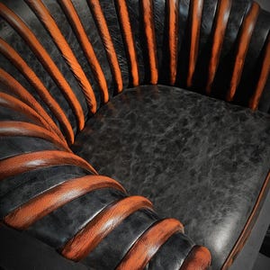 May include: A black leather armchair with orange leather accents. The chair has a unique design with the leather wrapped around the frame in a spiral pattern.