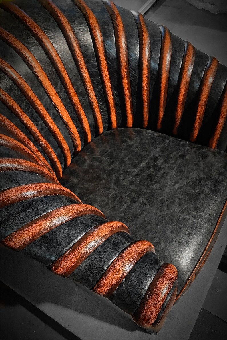 May include: A black leather armchair with orange leather accents. The chair has a unique design with the leather wrapped around the frame in a spiral pattern.