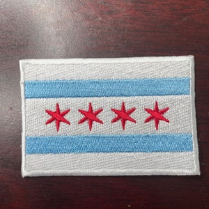 May include: A white embroidered patch with a blue stripe and four red six-pointed stars. The patch is a representation of the Chicago flag.