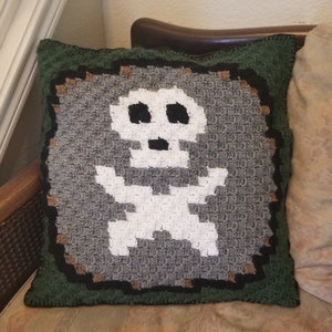 May include: A green, brown, and gray crocheted pillow with a white skeleton design.