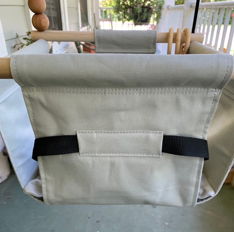 May include: A gray canvas swing seat with black straps. The swing is hanging from a wooden frame.
