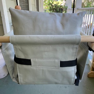 May include: A light gray canvas swing seat with a black strap and a matching light gray pillow. The swing seat is hanging from a wooden frame.