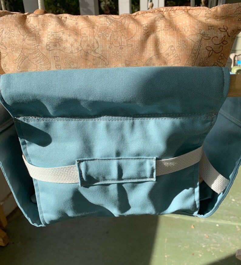 May include: A teal blue fabric swing seat with a white strap and a pocket. The seat is attached to a wooden frame.