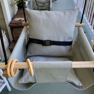 May include: A gray canvas swing seat with a gray cushion and a black safety strap. The swing has two wooden bars with wooden rings attached.