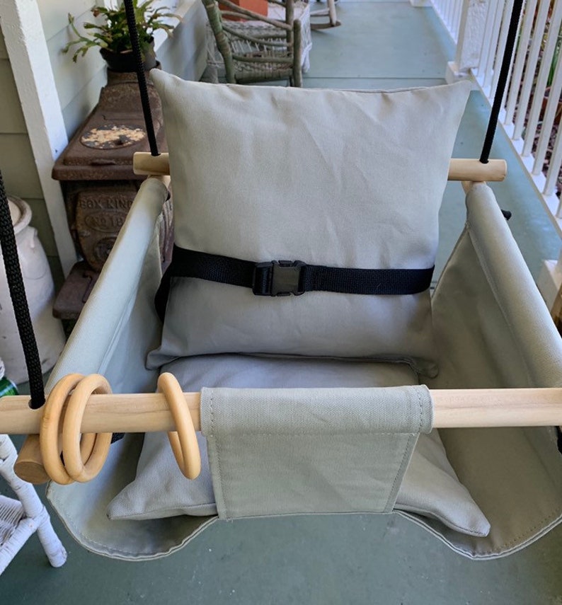 May include: A gray canvas swing seat with a gray cushion and a black safety strap. The swing has two wooden bars with wooden rings attached.
