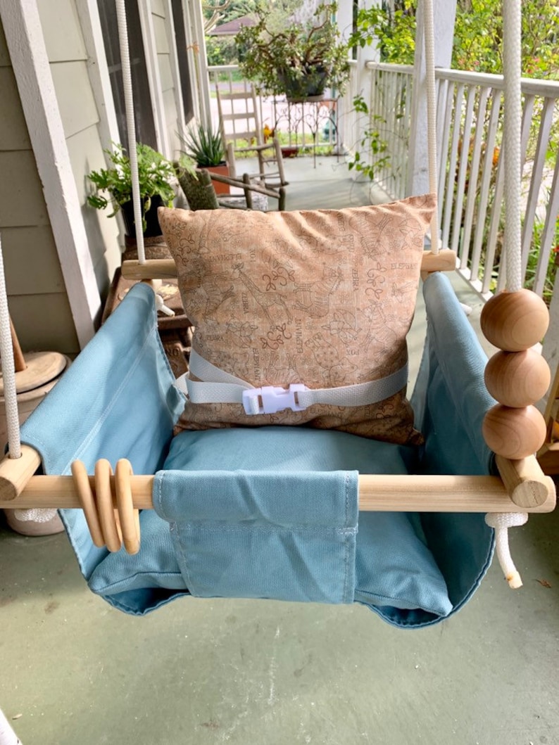 May include: A light blue baby swing with a wooden frame and a brown patterned pillow. The swing has a white rope and wooden beads.