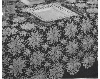 May include: A white crocheted tablecloth with a floral design. The tablecloth is laid out on a table with a white plate, silverware, and a glass.