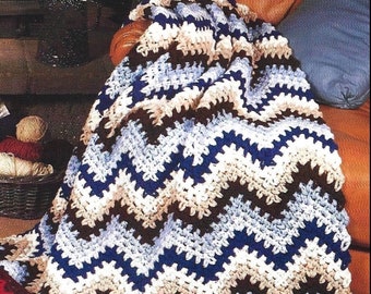 May include: A crocheted blanket with a chevron pattern in shades of brown, blue, and white. The blanket is draped over a chair and has a fringe border.