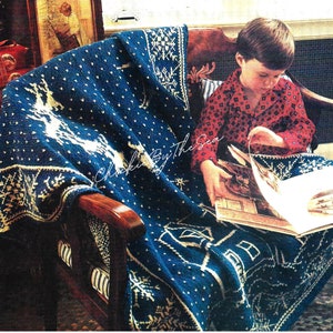 May include: A blue and white crocheted blanket with a snowflake and reindeer design. A child is sitting in a chair with the blanket draped over their lap, reading a book.