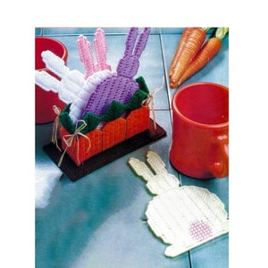 May include: A set of four crocheted bunny coasters, three in a basket and one on a tile floor. The basket is orange and brown with green trim. The bunnies are white, pink, and purple.