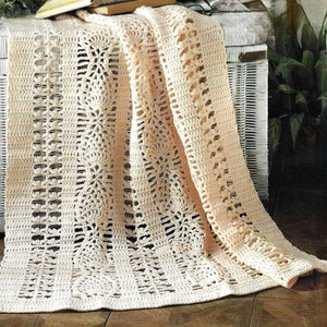 May include: A crocheted throw blanket in a cream color with a lacy pattern. The blanket is draped over a white wicker storage bench.
