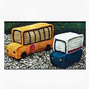 May include: Two crocheted toy vehicles, a yellow school bus with a red stop sign and a blue and white delivery truck. Both vehicles are sitting on a bed of gravel.