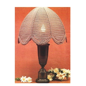 May include: A crocheted lampshade with a scalloped edge in a light brown color. The lampshade is on a dark brown lamp base with a floral design.