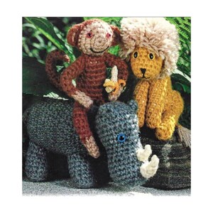 May include: A crocheted monkey, lion, and rhinoceros. The monkey is brown and holding a yellow banana. The lion is yellow with a white mane. The rhinoceros is gray with a blue eye.
