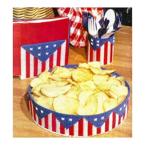 May include: A set of three red, white, and blue plastic canvas crafts featuring an American flag design. The crafts include a napkin holder, a utensil holder, and a chip and dip bowl.