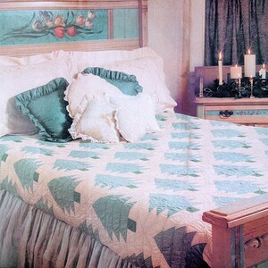 May include: A white bed with a blue and white quilt featuring a repeating pattern of stylised pine trees. The bed has a white headboard with a painted floral design and a white ruffled bed skirt. There are several white pillows with lace trim and a teal pillow on the bed.