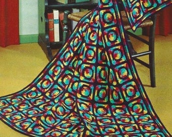 May include: A colourful crocheted blanket with a geometric pattern of squares and circles in shades of blue, yellow, red, and black. The blanket is draped over a wooden chair.