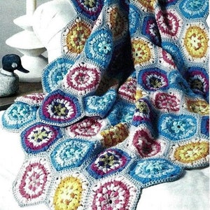 Pode incluir: Uma manta de crochê colorida e feita à mão. A manta apresenta um padrão repetitivo de formas hexagonais, cada uma com um design floral central em tons de amarelo, rosa, azul e branco. A manta está sobre uma superfície branca, mostrando os detalhes.