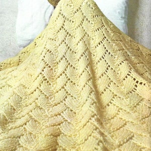 May include: A yellow crocheted blanket with a delicate openwork pattern. The blanket is draped over a bed and a person is partially visible under the blanket.