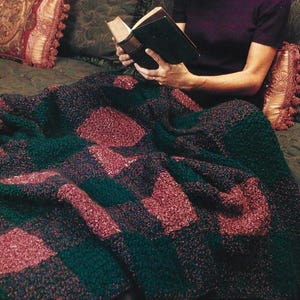 Könnte beinhalten: Eine handgefertigte Decke mit einem Schachbrettmuster. Die Decke hat abwechselnd dunkelgrüne und bordeauxfarbene Quadrate. Die Textur wirkt weich und einladend. Die Decke ist über ein Bett drapiert und suggeriert Komfort und Wärme.