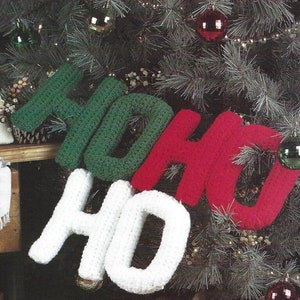 Może przedstawiać: Zielone, czerwone i białe szydełkowe litery tworzące napis "HO HO HO" wiszące na choince.