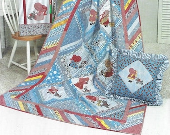Puede incluir: Una colcha de retazos azul y roja con un borde blanco. La colcha presenta un patrón repetitivo de niñas pequeñas con vestidos rojos y gorros blancos. La colcha se exhibe en una cómoda blanca con una almohada en el suelo.