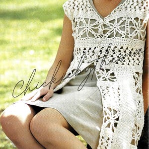 Può includere: Un gilet bianco all'uncinetto senza maniche con un motivo floreale. Il gilet ha una scollatura a V profonda ed è aperto sul davanti. La modella indossa il gilet sopra un abito grigio chiaro.