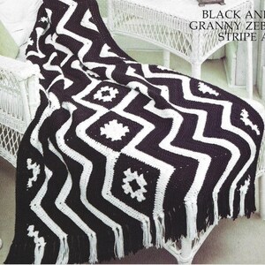 May include: Black and white crochet blanket with a chevron pattern and granny squares. The blanket has fringe on the edges.