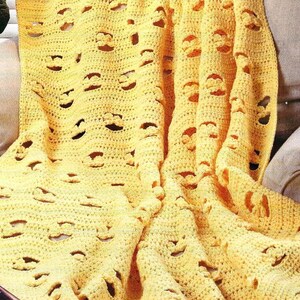 May include: A yellow crocheted blanket with a repeating pattern of openwork designs. The blanket is draped over a sofa, showcasing its texture and color. The handmade blanket is a cozy home decor item.