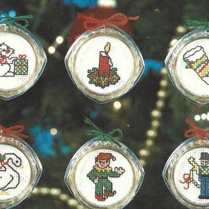 Peut inclure: Douze boules rondes en verre blanc avec des n&oelig;uds en ruban rouge et vert. Chaque boule pr&eacute;sente un motif de point de croix diff&eacute;rent, notamment un cheval &agrave; bascule, un lapin, une bougie, une chaussette, un chien, un cygne, un clown, un casse-noisette et un bonhomme de neige.