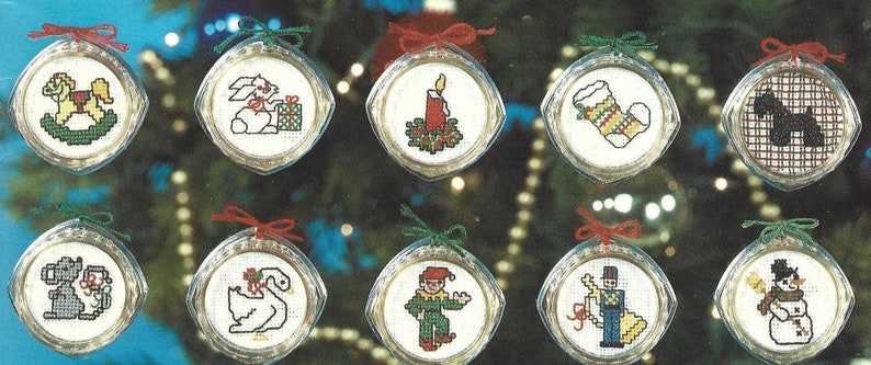 Peut inclure: Douze boules rondes en verre blanc avec des n&oelig;uds en ruban rouge et vert. Chaque boule pr&eacute;sente un motif de point de croix diff&eacute;rent, notamment un cheval &agrave; bascule, un lapin, une bougie, une chaussette, un chien, un cygne, un clown, un casse-noisette et un bonhomme de neige.