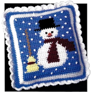 May include: A crocheted pillow featuring a snowman with a black hat, red scarf, and a broom. The snowman is on a blue background with white dots representing snow.