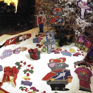 Puede incluir: Una falda de árbol de Navidad con adornos de punto de cruz. Presenta un soldado de juguete, un ratón con uniforme y una bailarina. Bastones de caramelo, cupcakes y caramelos envueltos también están dispersos, con un borde rojo.