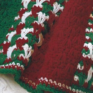 May include: A crocheted blanket with a red, white, and green design. The blanket is made with a textured stitch and has a scalloped edge.
