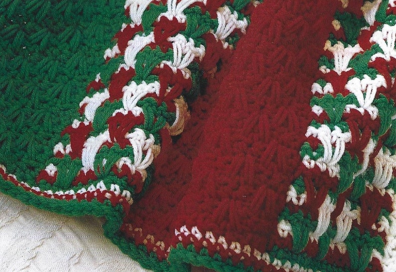 May include: A crocheted blanket with a red, white, and green design. The blanket is made with a textured stitch and has a scalloped edge.