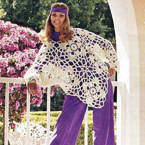 May include: A white crocheted poncho with a lacy design. The poncho is worn over a purple top and purple trousers.